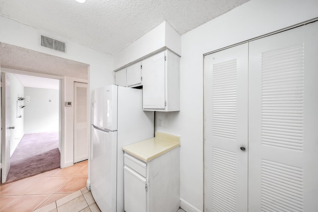 kitchen with visible vents, light carpet, light countertops, white cabinets, and freestanding refrigerator