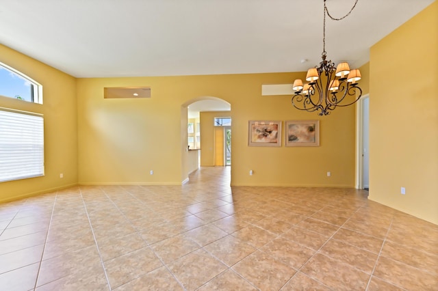 spare room with arched walkways, light tile patterned floors, and a chandelier