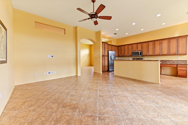 kitchen featuring appliances with stainless steel finishes, arched walkways, a ceiling fan, brown cabinetry, and light tile patterned floors