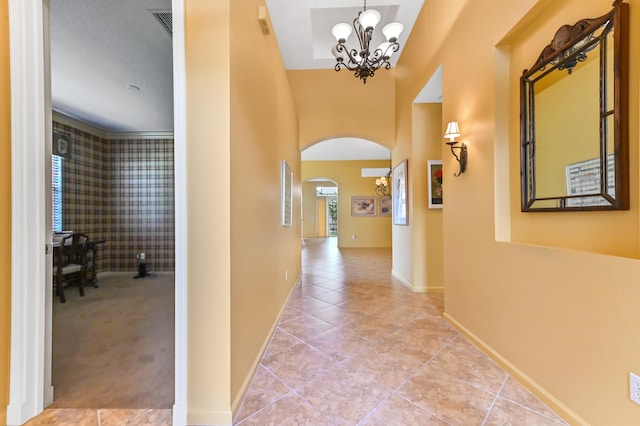 hallway with arched walkways, a chandelier, tile patterned floors, and baseboards