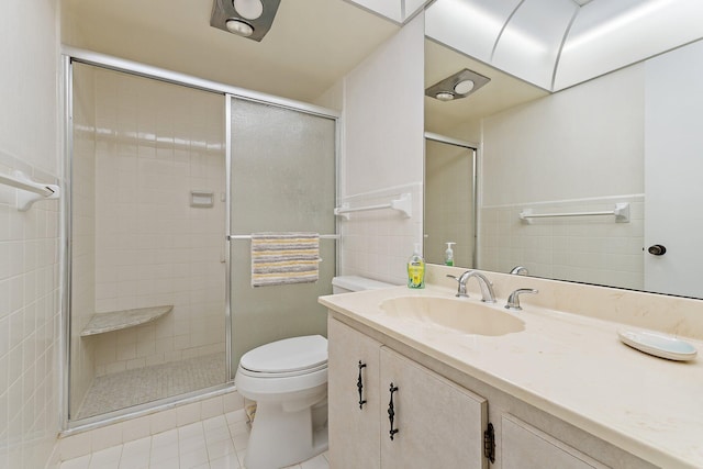 bathroom featuring tile patterned flooring, vanity, toilet, tile walls, and a shower stall