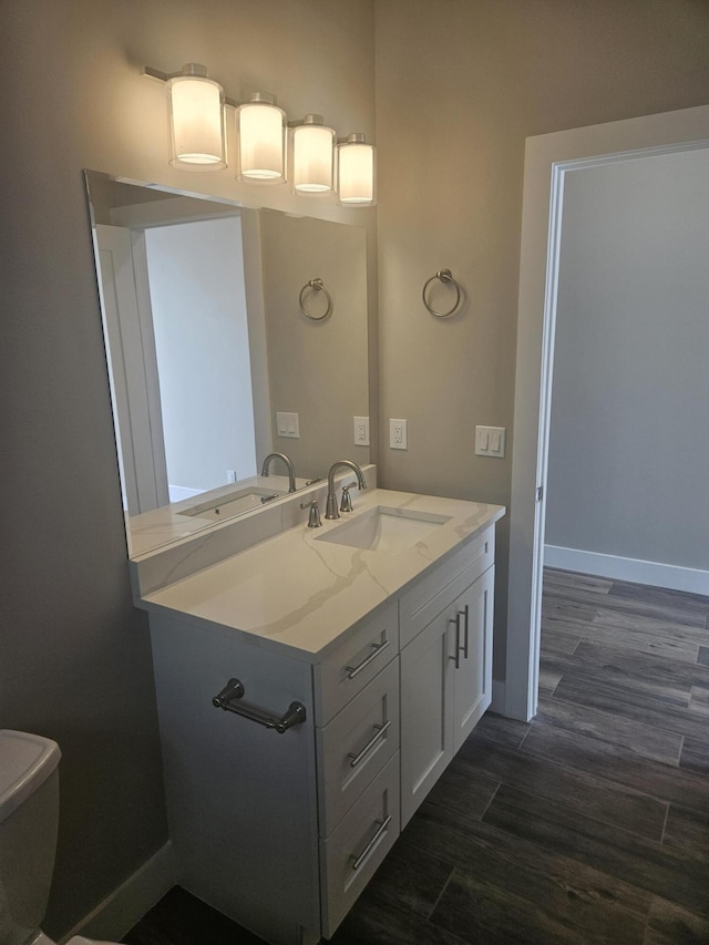bathroom featuring baseboards, wood finished floors, toilet, and vanity