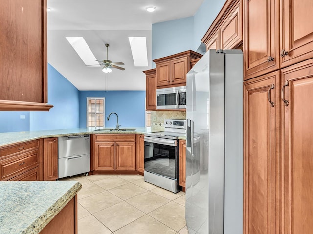 kitchen with brown cabinetry, vaulted ceiling with skylight, a sink, appliances with stainless steel finishes, and light tile patterned floors