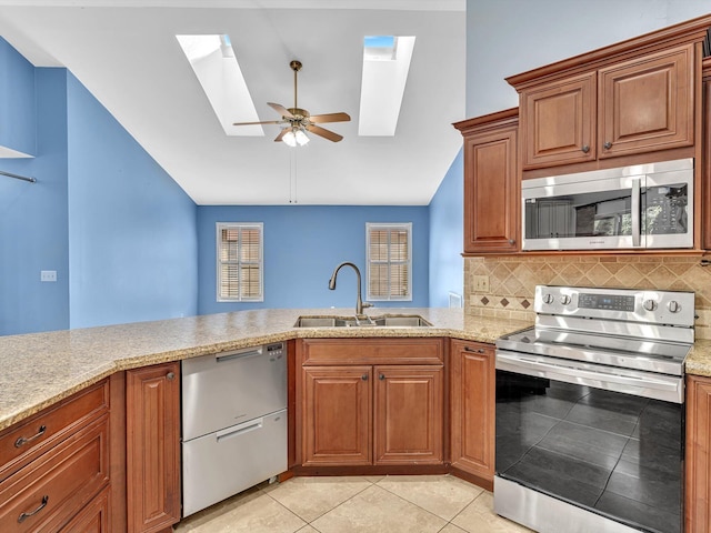 kitchen with light stone countertops, appliances with stainless steel finishes, a sink, and lofted ceiling with skylight