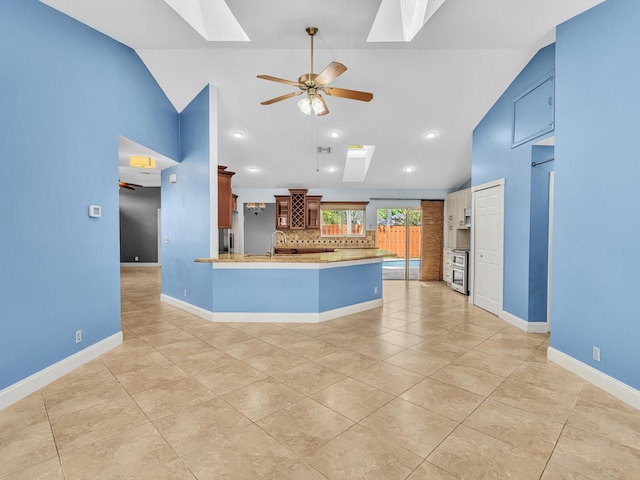 kitchen featuring light tile patterned flooring, ceiling fan, a peninsula, decorative backsplash, and a skylight