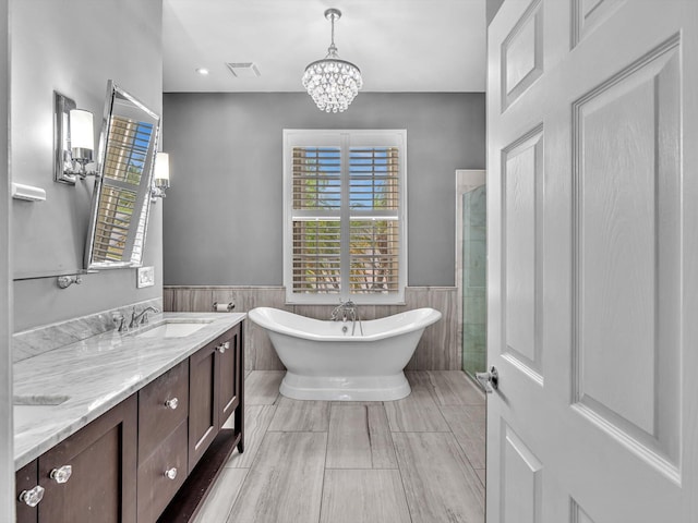 bathroom featuring double vanity, wainscoting, a freestanding tub, a chandelier, and a sink
