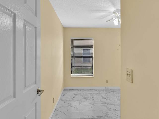 unfurnished room with a textured ceiling, ceiling fan, baseboards, and marble finish floor
