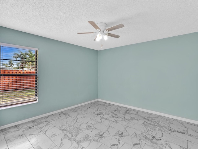 spare room featuring a ceiling fan, baseboards, marble finish floor, and a textured ceiling