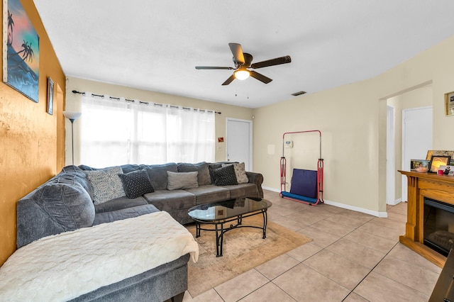 living room featuring light tile patterned floors, a glass covered fireplace, baseboards, visible vents, and a ceiling fan