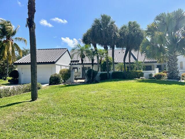 view of front of property featuring a tiled roof, an attached garage, stucco siding, and a front lawn