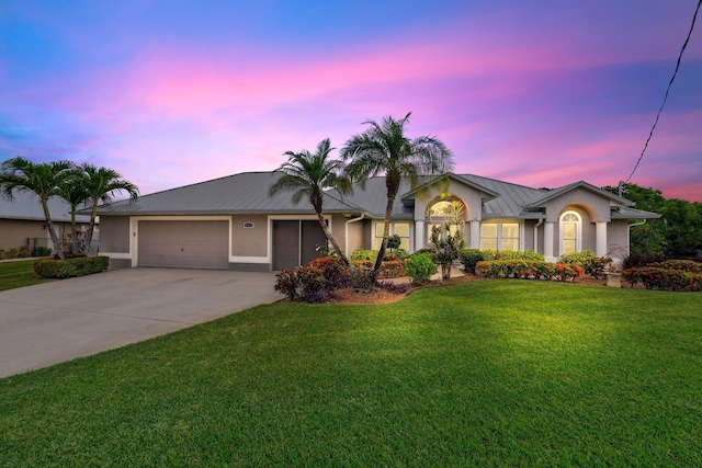 ranch-style house featuring a garage, stucco siding, metal roof, concrete driveway, and a front yard
