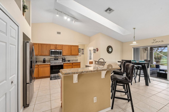 kitchen featuring brown cabinetry, light tile patterned floors, visible vents, a kitchen bar, and appliances with stainless steel finishes