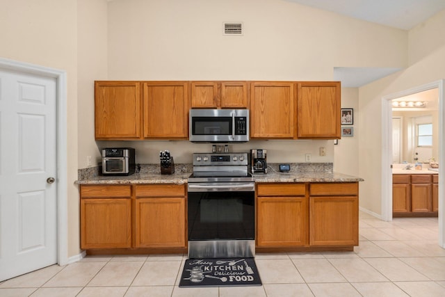 kitchen with light stone countertops, brown cabinetry, visible vents, light tile patterned flooring, and appliances with stainless steel finishes
