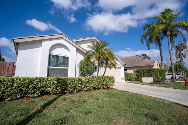 view of property exterior featuring fence, an attached garage, stucco siding, a lawn, and driveway
