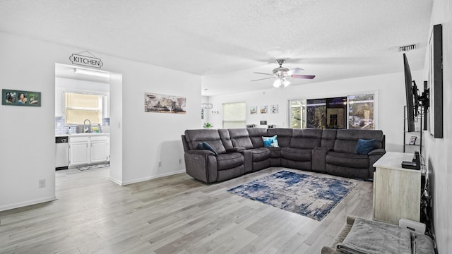 living room with a ceiling fan, a textured ceiling, visible vents, baseboards, and light wood-style flooring
