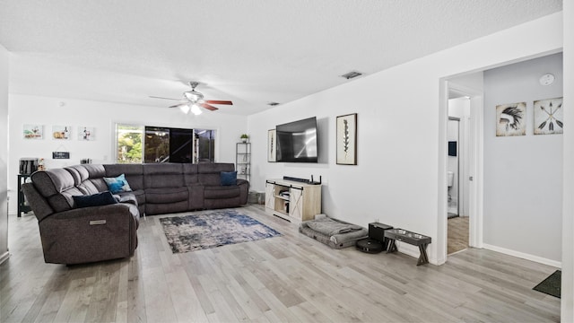 living area featuring a textured ceiling, ceiling fan, visible vents, and light wood-style flooring