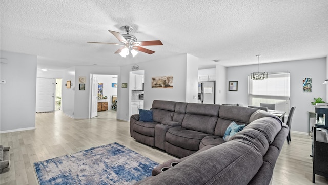 living area with light wood-style floors, a ceiling fan, a textured ceiling, and baseboards