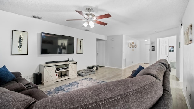 living room featuring light wood-style floors, a textured ceiling, a ceiling fan, baseboards, and visible vents