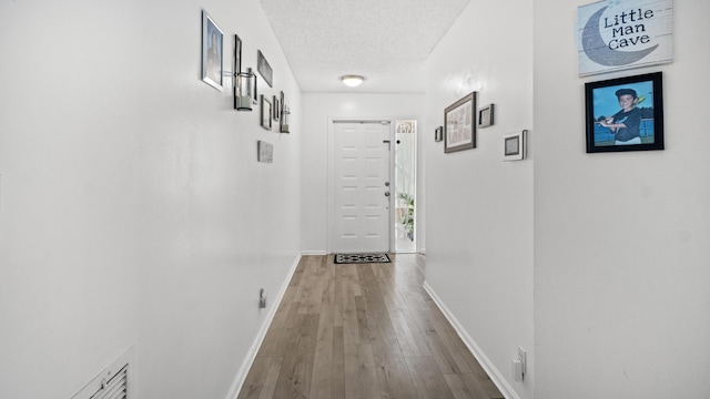 hall with a textured ceiling, baseboards, and hardwood / wood-style floors