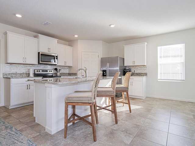 kitchen featuring a kitchen island with sink, stainless steel appliances, backsplash, white cabinetry, and a kitchen breakfast bar