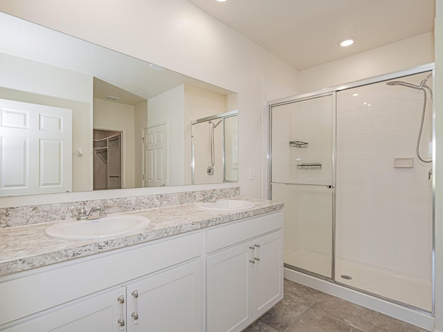 bathroom featuring double vanity, a walk in closet, a stall shower, and a sink