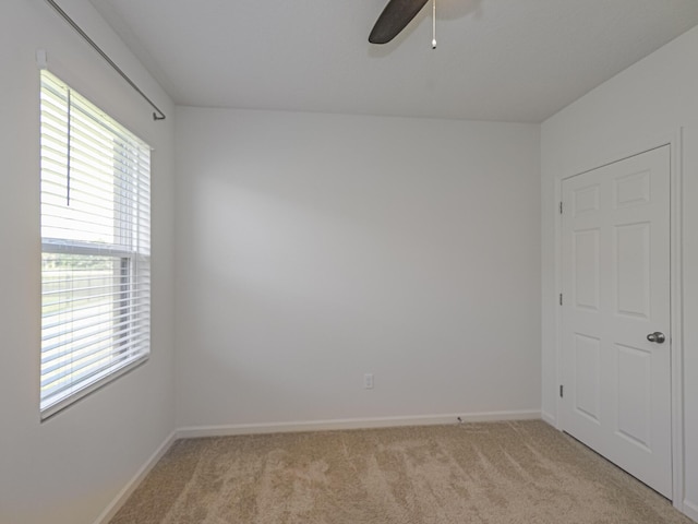 empty room featuring a ceiling fan, light colored carpet, and plenty of natural light