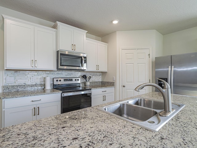 kitchen featuring a sink, decorative backsplash, white cabinetry, a textured ceiling, and appliances with stainless steel finishes