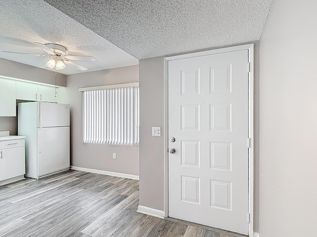 kitchen with light wood-style flooring, freestanding refrigerator, ceiling fan, baseboards, and a textured ceiling