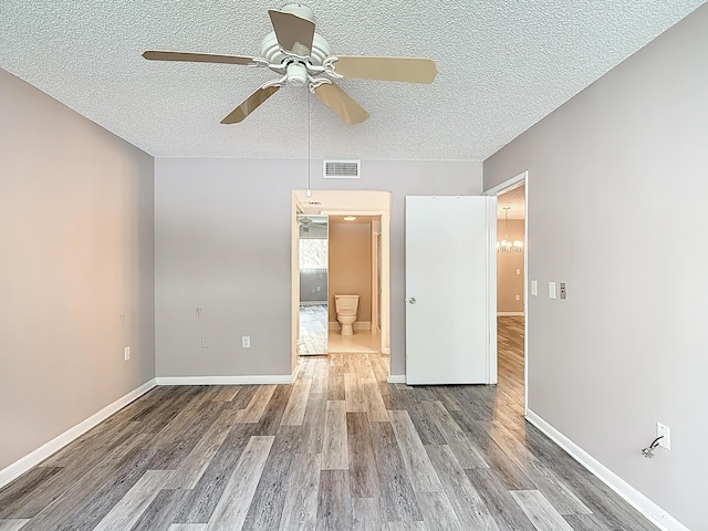 empty room with visible vents, wood finished floors, ceiling fan, and a textured ceiling