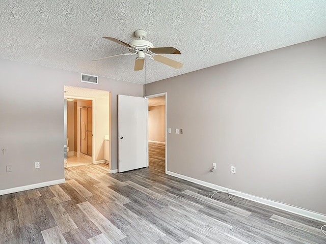 unfurnished bedroom with a textured ceiling, visible vents, wood finished floors, and baseboards