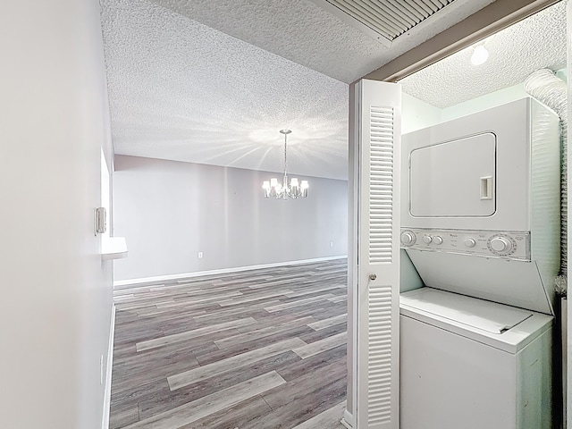clothes washing area featuring a textured ceiling, wood finished floors, stacked washer / dryer, and laundry area