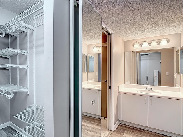 bathroom with a textured ceiling, wood finished floors, vanity, and baseboards