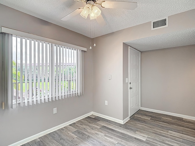 spare room featuring a textured ceiling, ceiling fan, wood finished floors, and visible vents