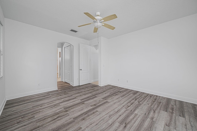 spare room featuring visible vents, baseboards, arched walkways, wood finished floors, and a ceiling fan