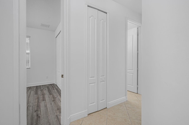 hall featuring light tile patterned flooring, visible vents, and baseboards