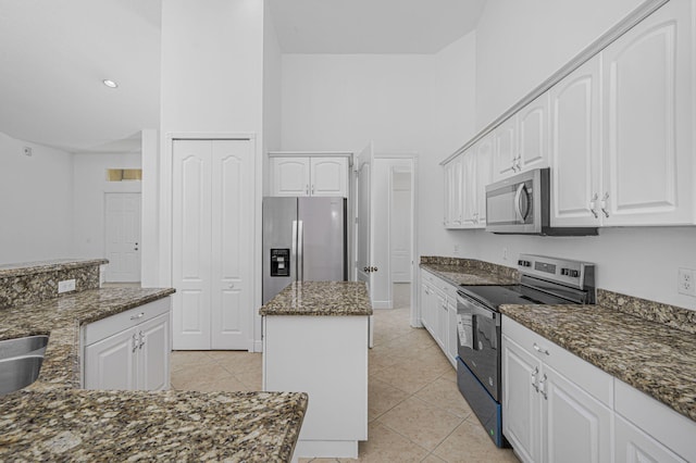kitchen featuring dark stone counters, light tile patterned flooring, a center island, white cabinetry, and appliances with stainless steel finishes