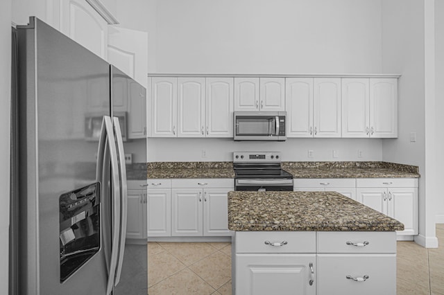 kitchen with light tile patterned floors, dark stone countertops, appliances with stainless steel finishes, and white cabinetry
