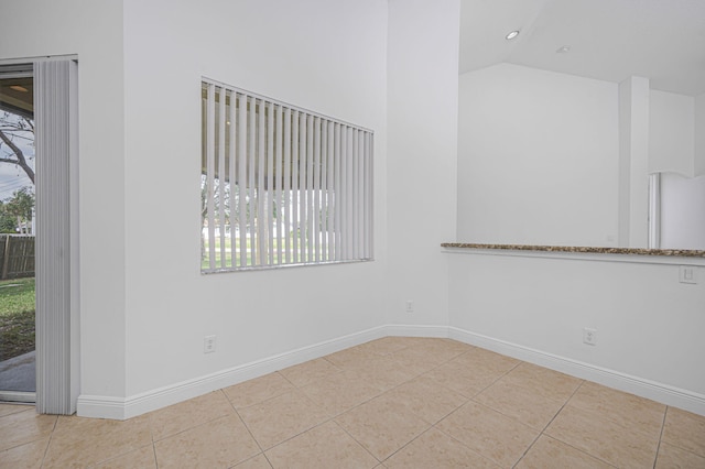 tiled empty room with vaulted ceiling and baseboards