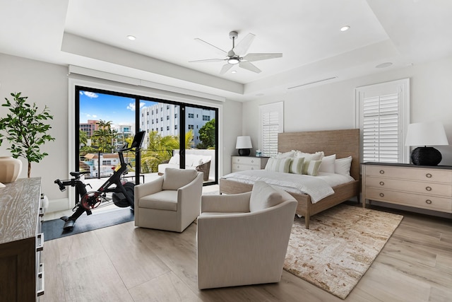 bedroom with a raised ceiling, a ceiling fan, light wood-style floors, and access to exterior