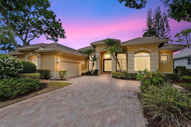 mediterranean / spanish-style home with decorative driveway, a garage, stucco siding, and a tiled roof