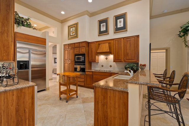 kitchen featuring ornamental molding, built in appliances, a peninsula, premium range hood, and a sink