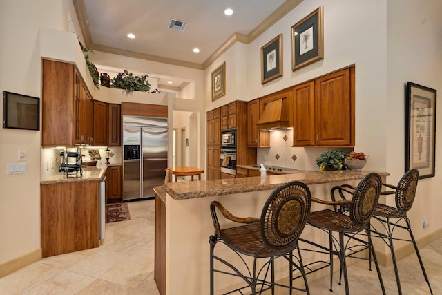 kitchen with built in appliances, premium range hood, a peninsula, visible vents, and ornamental molding