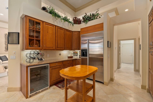 kitchen featuring glass insert cabinets, beverage cooler, baseboards, stainless steel built in fridge, and light stone counters