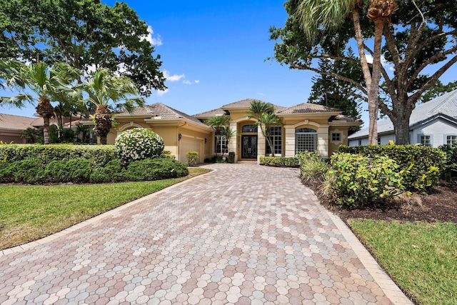 mediterranean / spanish-style home with stucco siding, decorative driveway, a tile roof, and a garage