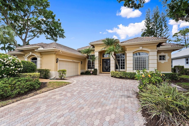 mediterranean / spanish house with a tiled roof, decorative driveway, a garage, and stucco siding
