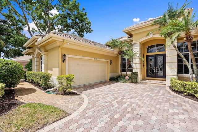 view of front of property featuring a garage, decorative driveway, stucco siding, and french doors