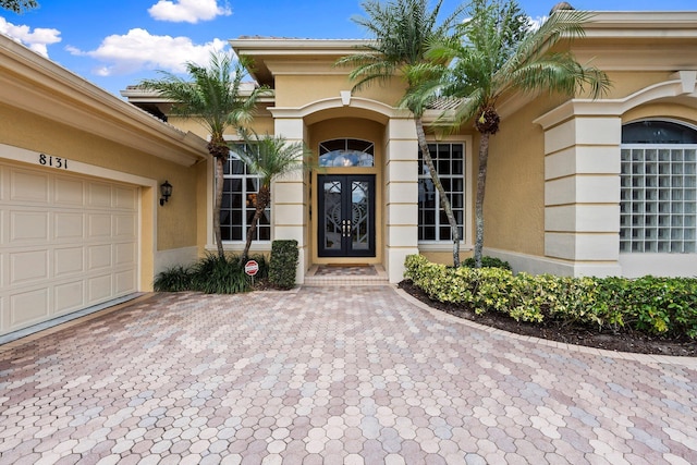 doorway to property featuring decorative driveway, a garage, french doors, and stucco siding