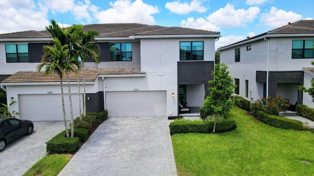 view of front facade with a front lawn, stucco siding, decorative driveway, a tiled roof, and an attached garage