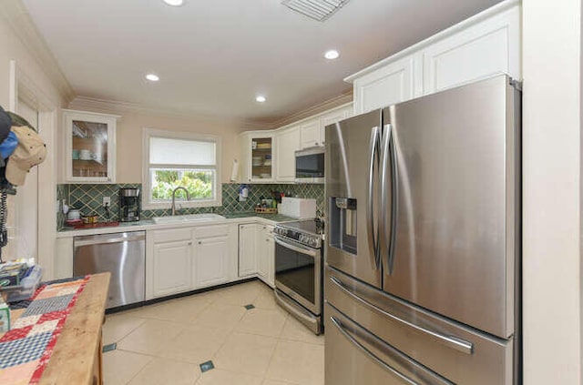 kitchen featuring glass insert cabinets, decorative backsplash, appliances with stainless steel finishes, white cabinets, and a sink