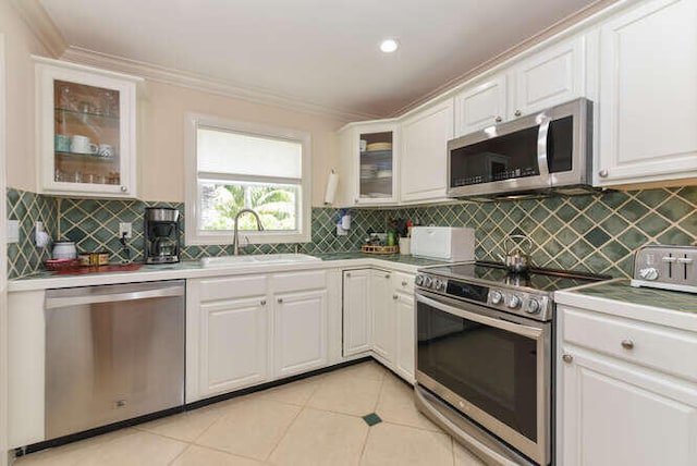 kitchen featuring light tile patterned floors, appliances with stainless steel finishes, white cabinets, ornamental molding, and a sink